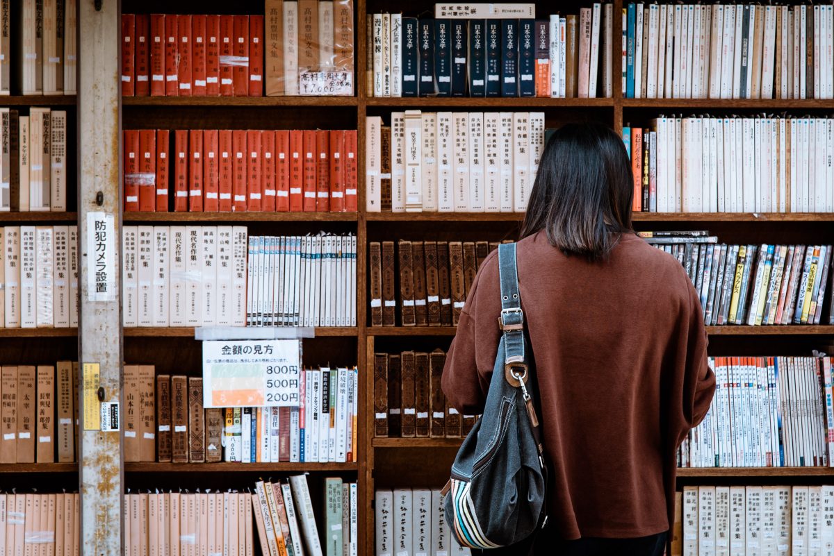 Eine Person, die in einer Bibliothek vor einer Regalwand voller Bücher steht
