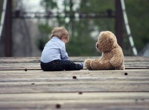 Ein Kind und ein Teddybär auf einem Holzboden draußen